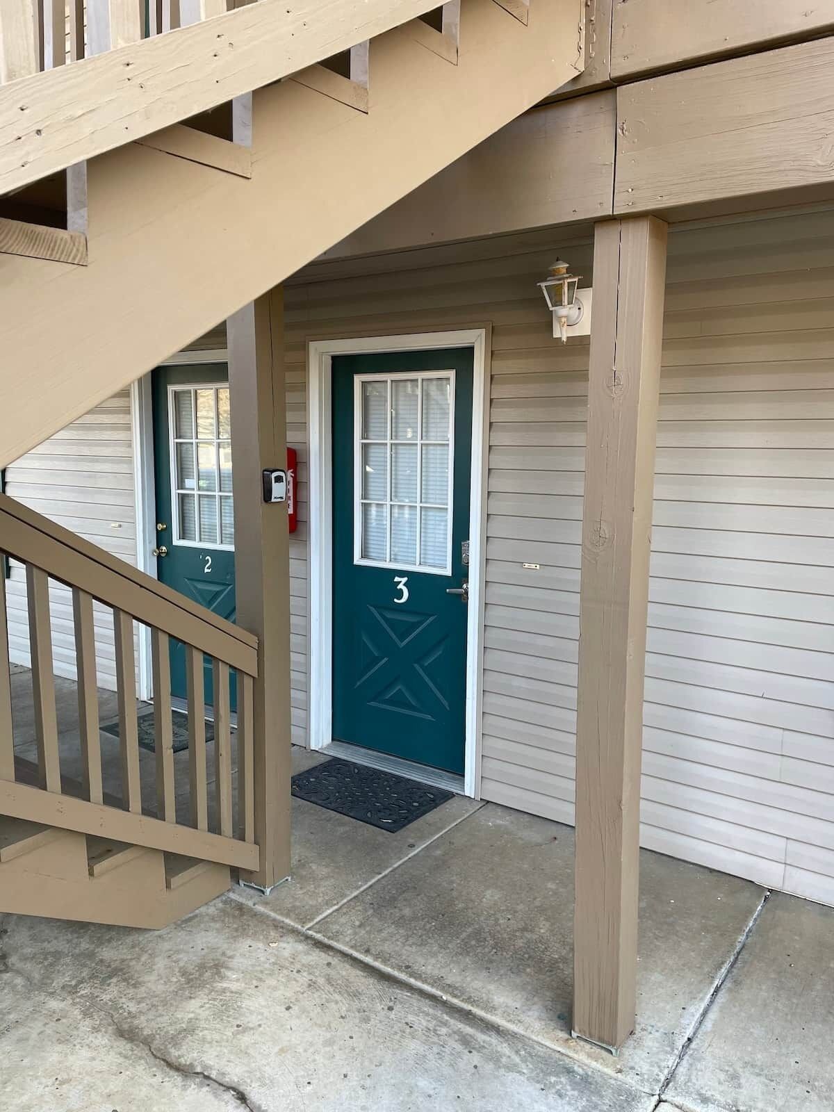 A building entrance with a green door marked '3', a mailbox, and a staircase leading to an upper level.