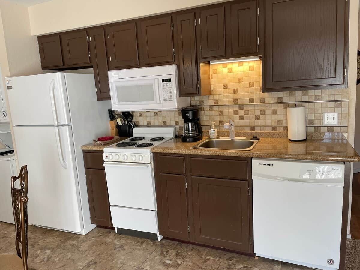A kitchen with brown cabinets, a white refrigerator, a microwave, a stove, a sink, and a dishwasher.