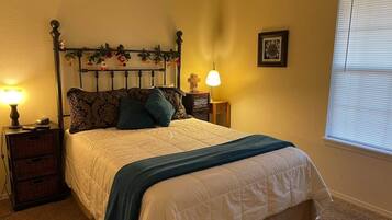 A bedroom with a four-poster bed, two bedside tables, a lamp, and a window with blinds.