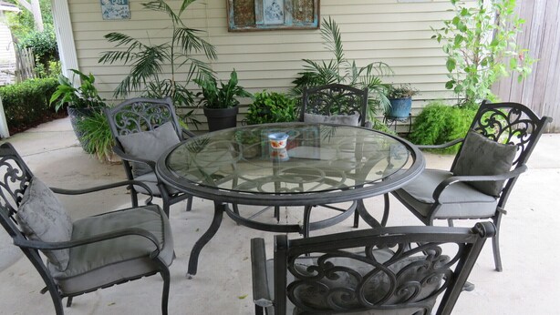 A round glass table with six metal chairs, surrounded by potted plants and a wooden fence.