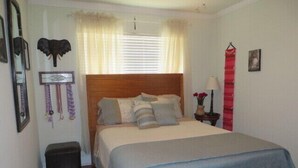 A bedroom with a wooden headboard, a bed with multiple pillows, a nightstand with a lamp, and a window with curtains.