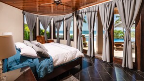 A bedroom with a large bed, a ceiling fan, and a view of the ocean through curtains.