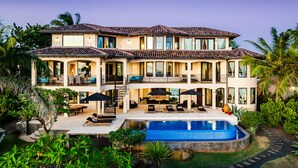 A multi-story house with a swimming pool, outdoor seating, and lush landscaping.
