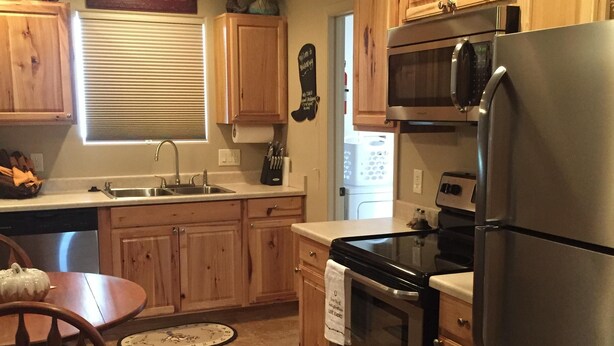 A kitchen with wooden cabinets, a stainless steel refrigerator, an oven, and a microwave. There is a sink with a window above it, and a sign on the wall that says "Live Laugh Love." -  Casita only 3 blocks from downtown- Very clean! (Wickenburg)