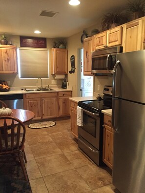 A kitchen with wooden cabinets, a stainless steel refrigerator, an oven, and a microwave. There is a sink with a window above it, and a sign on the wall that says "Live Laugh Love." - Casita only 3 blocks from downtown- Very clean! (Wickenburg)