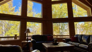 A cabin with large windows, a wooden ceiling, a sofa, a table, and a lamp.