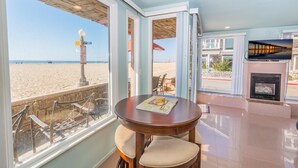 A beachfront room with a dining table, chairs, a fireplace, and a large window offering a view of the beach and ocean.