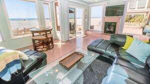 A spacious living room with a large glass door leading to a balcony, a fireplace, and a view of the beach.