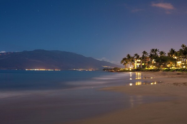 Un hotel frente a la playa con vista al océano y montañas al fondo.