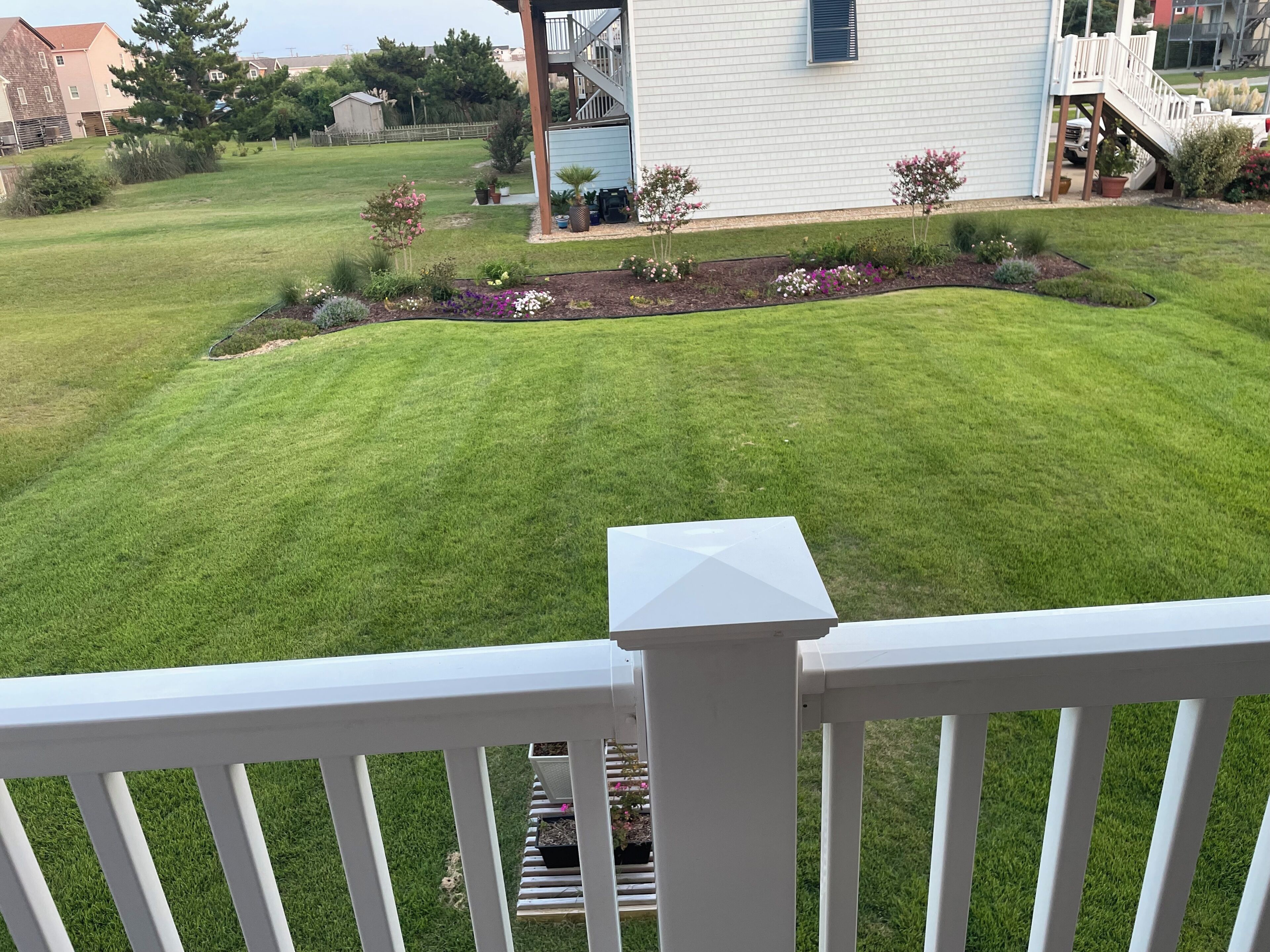 A well-maintained lawn with a small flower bed, a white railing, and a house in the background.