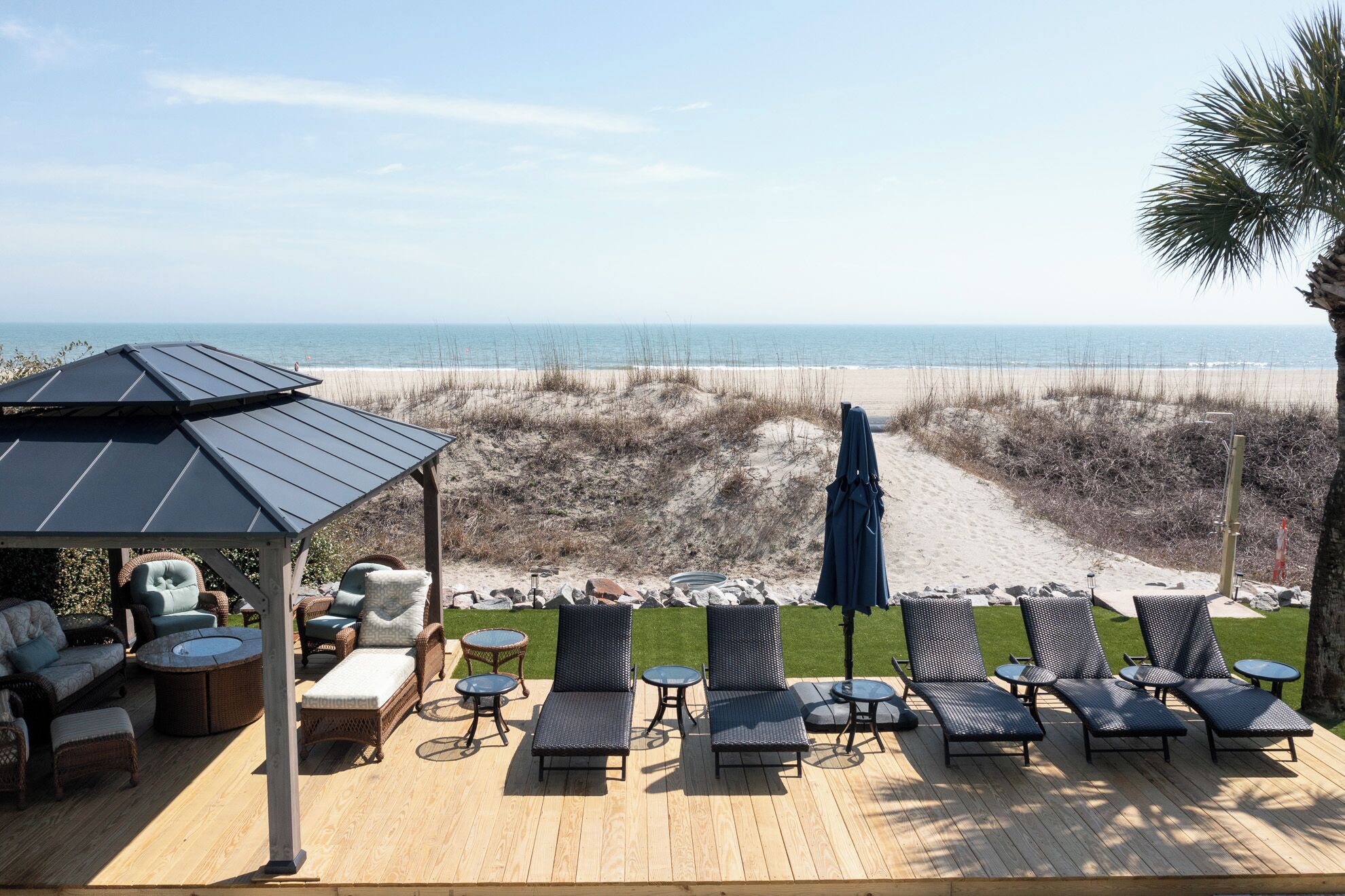 Un patio frente a la playa con sillones reclinables, una zona de estar techada y vista al océano.