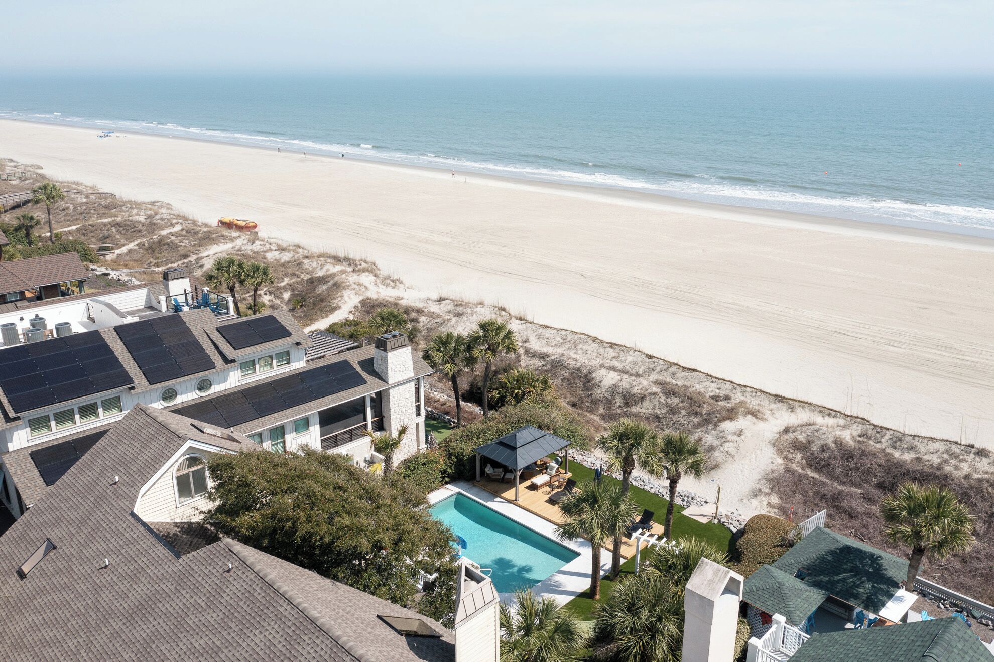 A beachfront property with solar panels, a swimming pool, and a beach view.