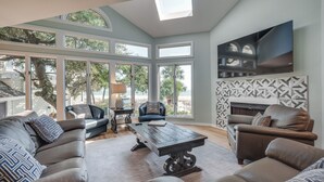 A spacious living room with a large window, a fireplace, and a television mounted on the wall.