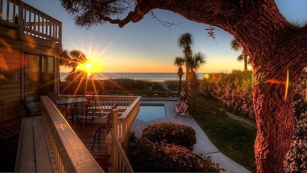 A wooden deck with outdoor furniture, a pool, and a large tree.