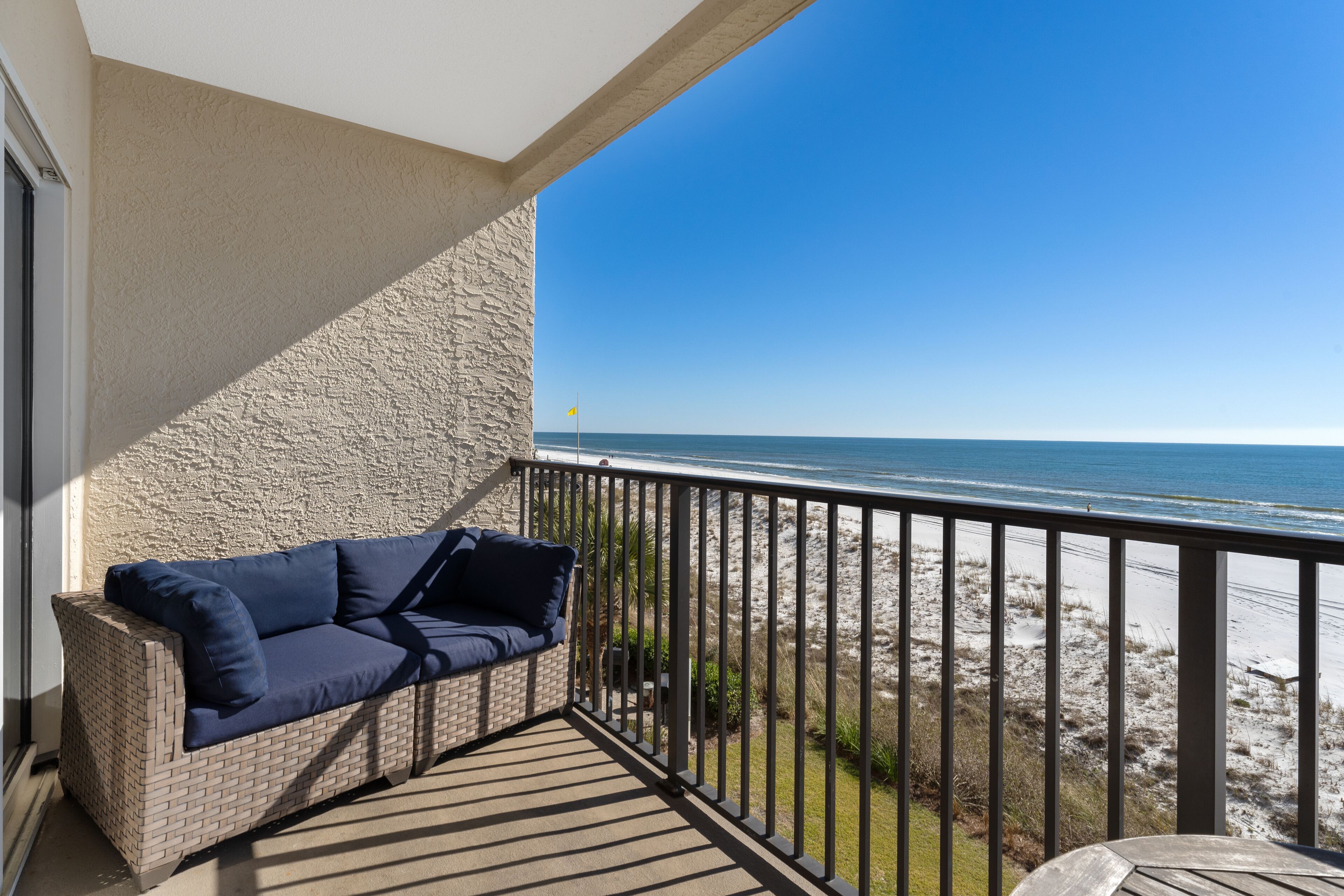 A balcony with a wicker sofa and a view of the beach.