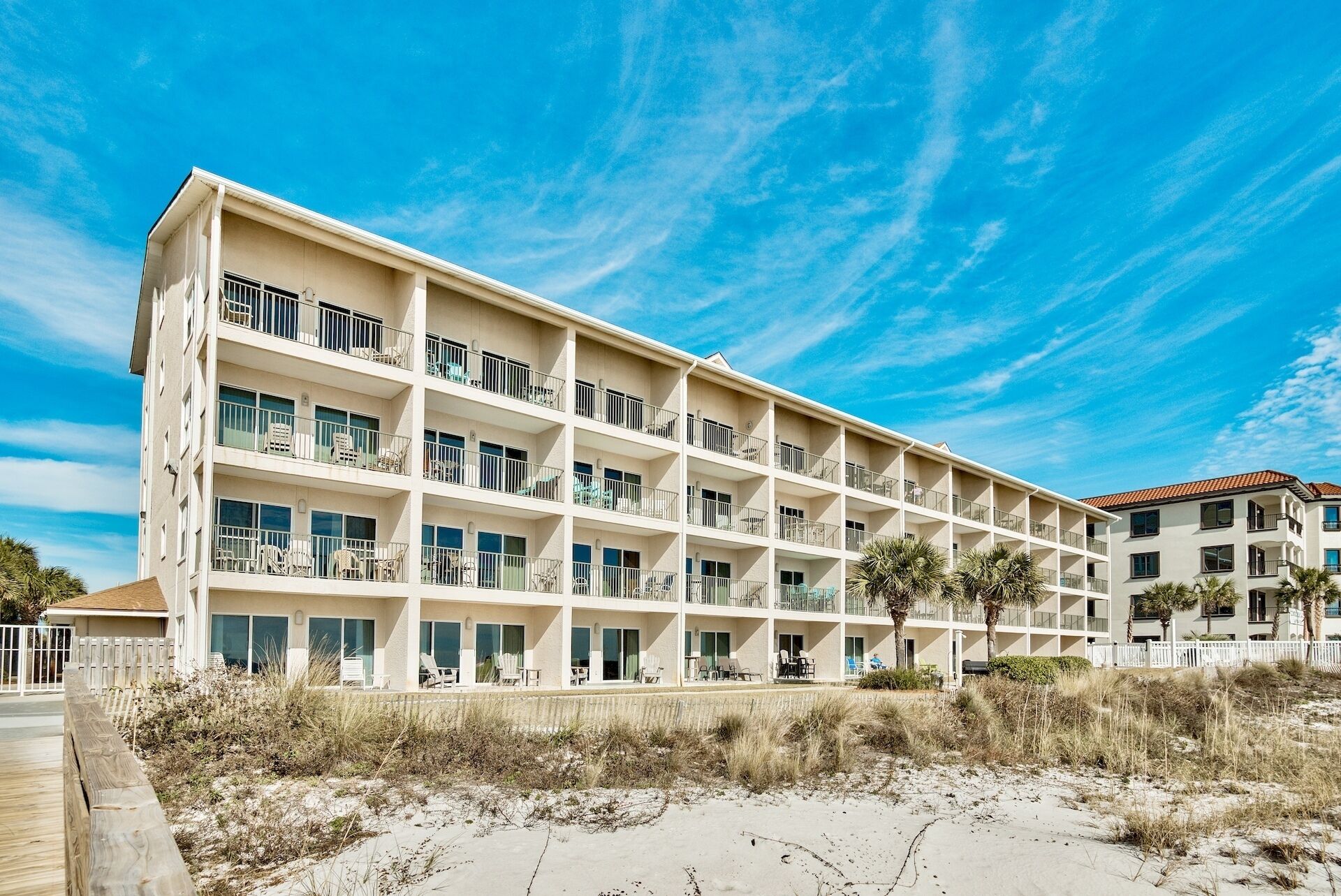 A multi-story hotel with balconies, located near a sandy beach.