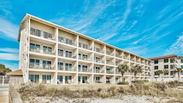 A multi-story hotel with balconies, located near a sandy beach.