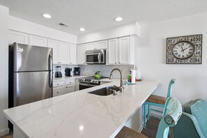 A modern kitchen with white cabinetry, stainless steel appliances, and a marble countertop.