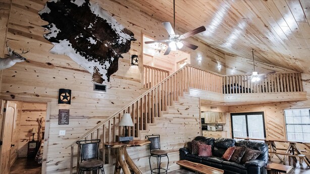 A wooden interior with a staircase, a black leather sofa, and a ceiling fan. - Casa Rio Hideaway @ Casa Rio Rentals- Pet Friendly with River access (Concan)