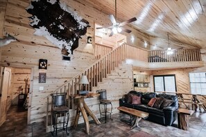 A wooden interior with a staircase, a black leather sofa, and a ceiling fan. - Casa Rio Hideaway @ Casa Rio Rentals- Pet Friendly with River access (Concan)
