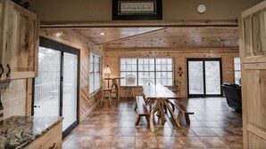 A spacious dining area with a wooden table and benches, large windows, and a framed sign on the wall. - Casa Rio Hideaway @ Casa Rio Rentals- Pet Friendly with River access (Concan)
