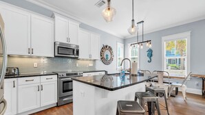 A modern kitchen with white cabinets, stainless steel appliances, a central island with stools, pendant lighting, and decorative wall art. - 2 Master Suites, 4 Bedroom,  Five ★ Home, Gourmet Kitchen - short walk to beach (Santa Rosa Beach)