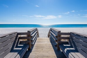 Una passerella di legno conduce a una spiaggia sotto un cielo azzurro terso.