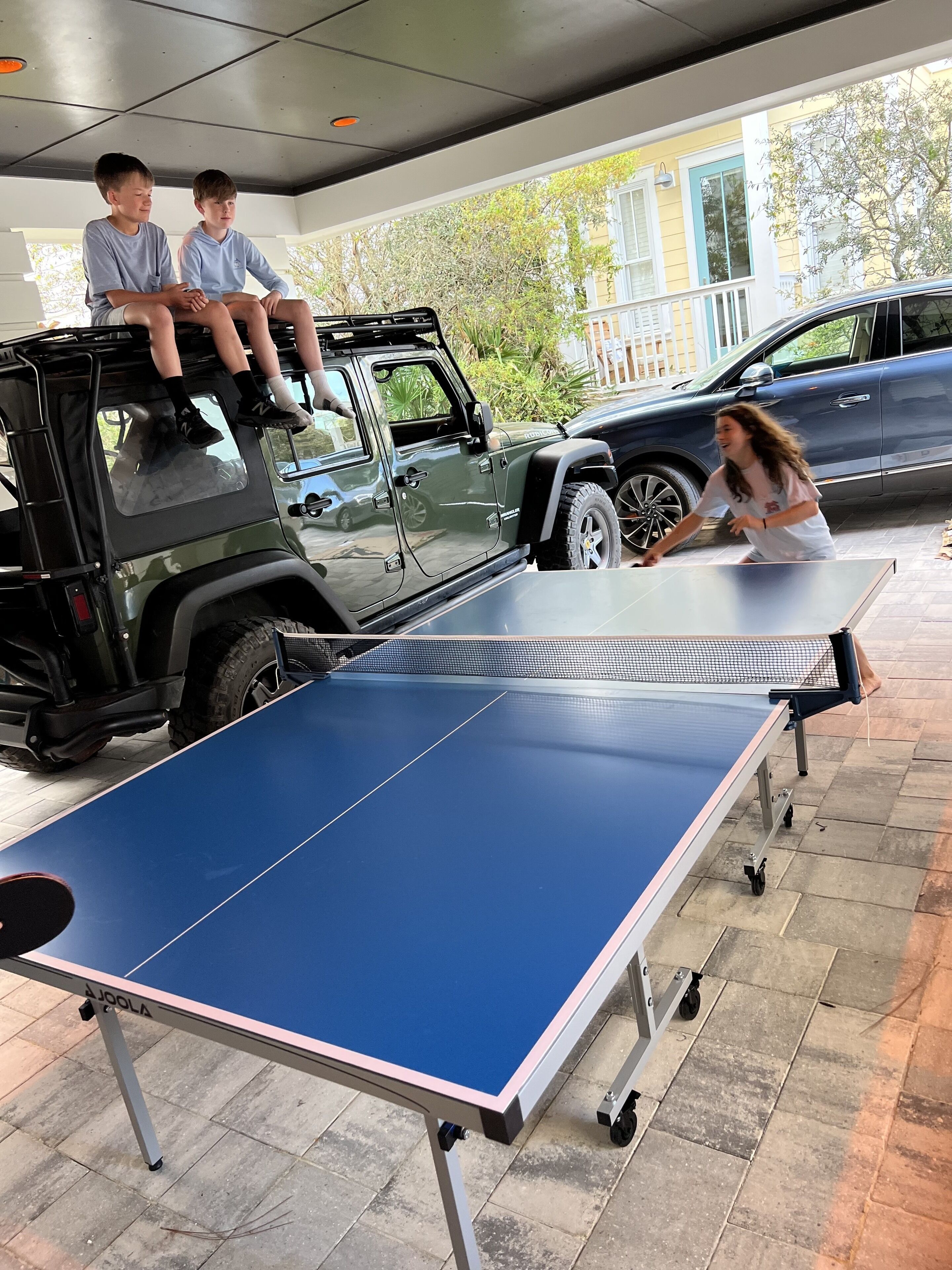 A table tennis table set up outdoors with a vehicle and a person playing.