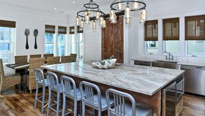 Una cocina con una isla grande, taburetes de bar, un lavamanos y una puerta de madera.