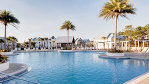 En swimmingpool med palmer och solstolar, omgiven av byggnader med modern design.