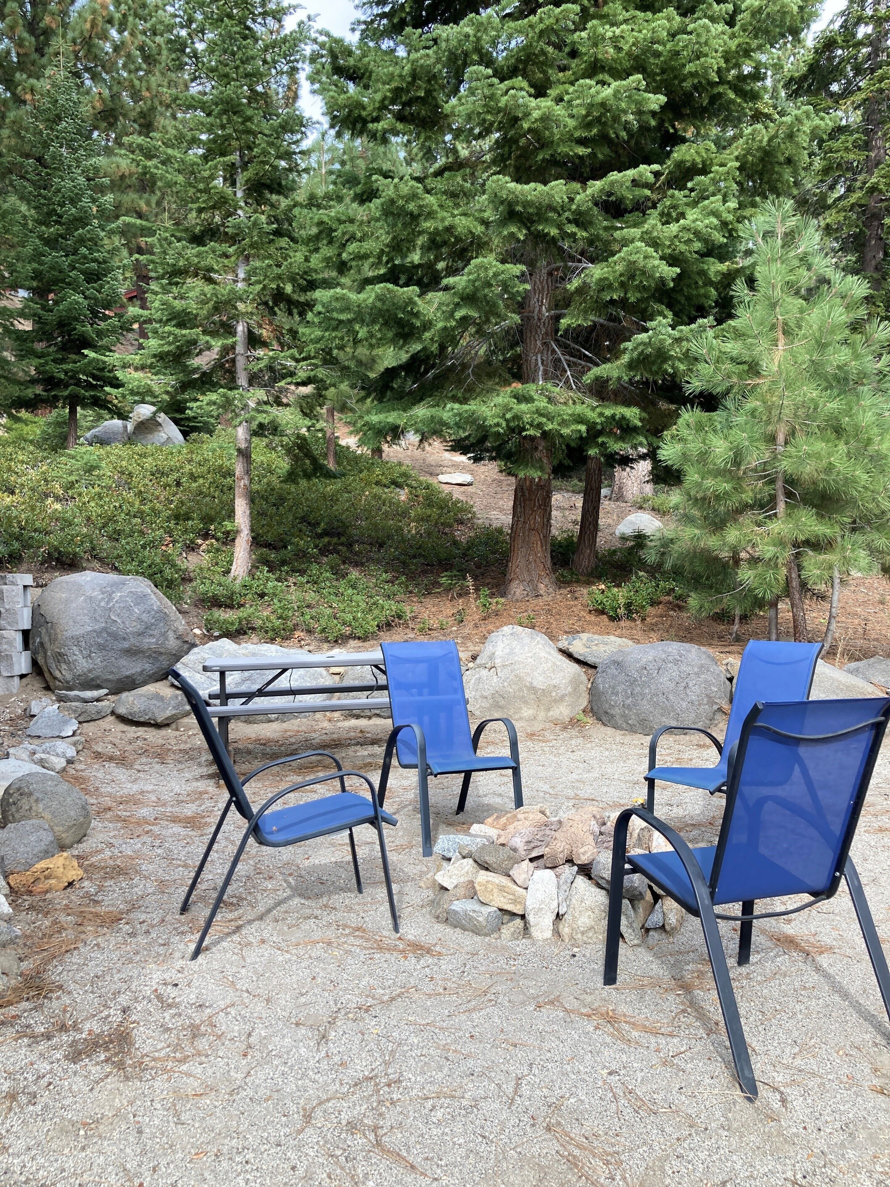 Een terras met een tafel en stoelen, omringd door rotsen en bomen.