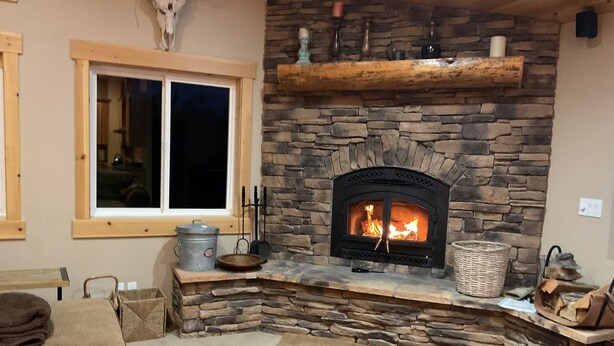 A cozy living room with a stone fireplace, a window with blinds, and a wooden coffee table.
