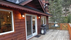 A wooden deck with a barbecue grill and a table, surrounded by a wooden fence and trees.