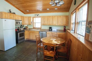 A kitchen with wooden cabinets, a refrigerator, stove, microwave, sink, and a dining table with chairs.