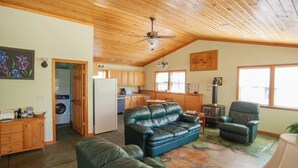 A cozy living area with a leather sofa, a chair, and a dining table. There's a kitchen with wooden cabinets and a stove.
