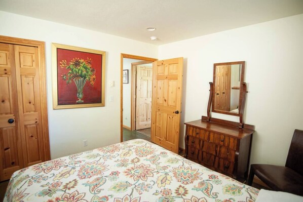 A bedroom with a bed, wooden wardrobe, dresser, mirror, and a painting on the wall.