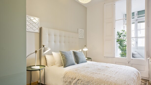 Een slaapkamer met een groot bed, twee bedlampen, een bed met een patroon en een raam met uitzicht op groen.