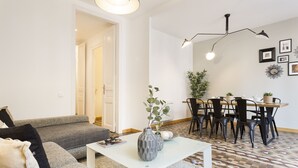 Een moderne woonkamer met een grijze bank, een witte salontafel, en een eethoek met een houten tafel en zwarte stoelen.