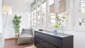 Een moderne kamer met een groot raam, een bank, een donker houten dressoir en een vloerlamp.