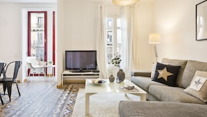 Een moderne woonkamer met een flatscreen televisie, een bank, een salontafel en een eethoek met stoelen.