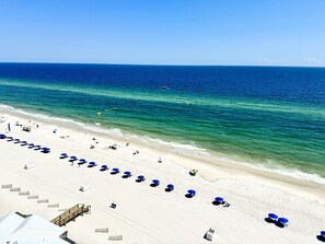 A beach with rows of blue umbrellas and sun loungers, a wooden walkway, and the ocean in the background. - Amazing Sunny Coastline View From 12th Floor. Pool & Direct Beach Access. (Gulf Shores)