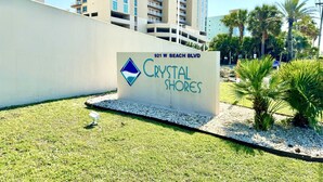 Een bord voor Crystal Shores, gelegen aan 921 W Beach Blvd, met een modern gebouw op de achtergrond.