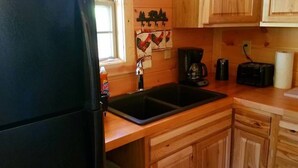 A kitchen with wooden cabinets, a black refrigerator, a sink, a coffee maker, and a toaster. - Private Ravine View Luxury Amish-Built Cabin "The Frontier" (Genoa)