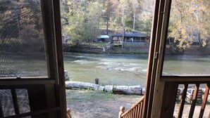 A view from a wooden deck overlooking a river, with a house and trees in the background. - RiverFront, WI-FI /Cell,  Pet Friendly, Folk School (Murphy)
