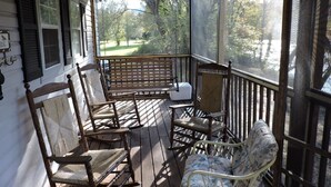 A porch with wooden rocking chairs and a white cushioned chair, overlooking a yard with trees. - RiverFront, WI-FI /Cell,  Pet Friendly, Folk School (Murphy)