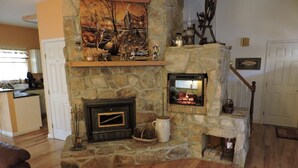 A stone fireplace with a built-in TV, a wooden floor, and a kitchen area in the background. - RiverFront, WI-FI /Cell,  Pet Friendly, Folk School (Murphy)