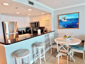A modern kitchen with stainless steel appliances, white cabinetry, and a dining area with a round table and bar stools. - August Beach Special! Direct Oceanfront Views @ SunDestin Resort (Destin)