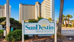 Un letrero de SunDestin Beach Resort con una vista despejada de edificios altos al fondo.