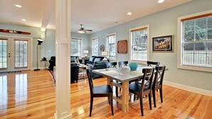 A spacious living room with a dining area, wooden floors, and large windows with blinds. - Airy & Bright Folly Condo; Close to Everything (Folly Beach)