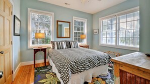 A bedroom with a bed, two bedside tables with lamps, a ceiling fan, and large windows with blinds. - Airy & Bright Folly Condo; Close to Everything (Folly Beach)